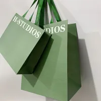 Les vêtements verts d'emballage chaussent les sacs en papier d'achats avec les poignées plates de ruban