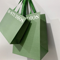 Les vêtements verts d'emballage chaussent les sacs en papier d'achats avec les poignées plates de ruban