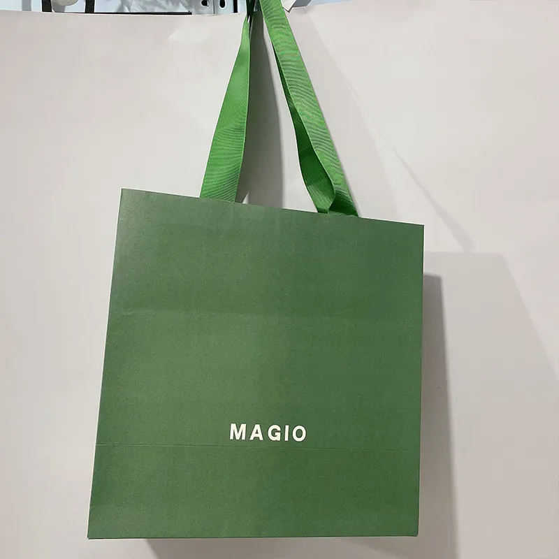 Les vêtements verts d'emballage chaussent les sacs en papier d'achats avec les poignées plates de ruban