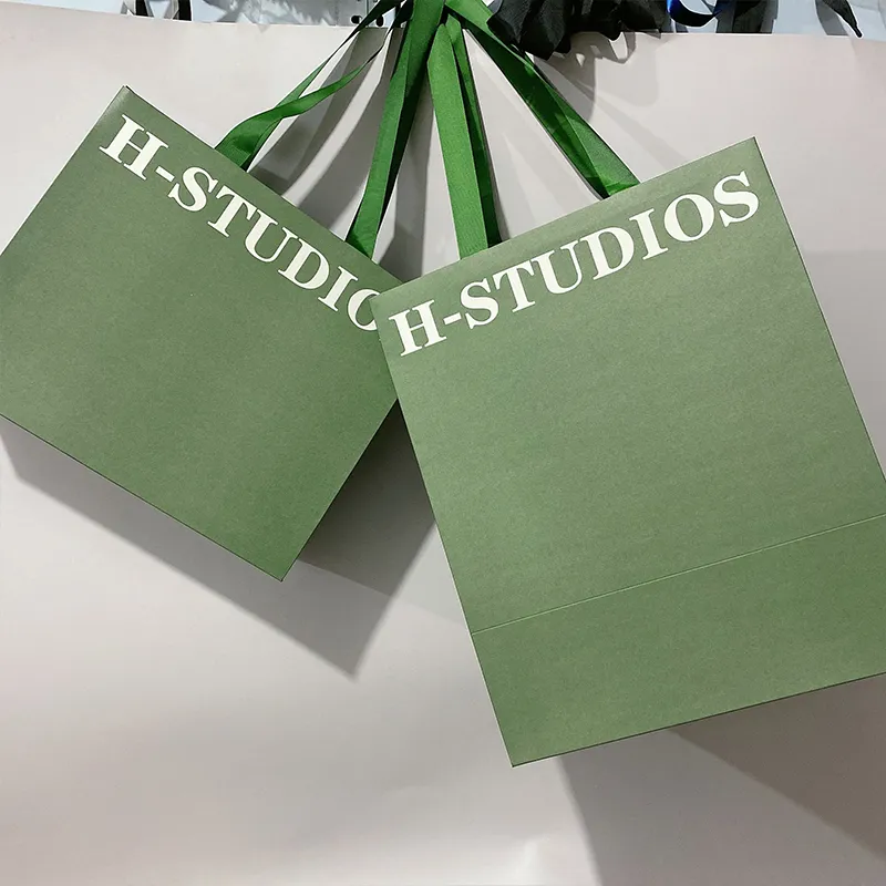 Les vêtements verts d'emballage chaussent les sacs en papier d'achats avec les poignées plates de ruban