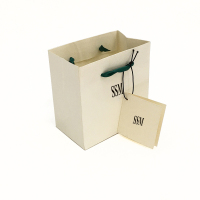 Маленькая упаковка сумки для гольфа из белой подарочной бумаги, пригодной для вторичной переработки, с именной биркой, ручками из зеленой ленты для декоративной упаковки ювелирных изделий.