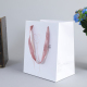 Recycelbare mittelgroße Luxus-Einkaufstaschen aus glänzend weißem Euro-Tragepapier mit schickem lila Seilgriff und Logo